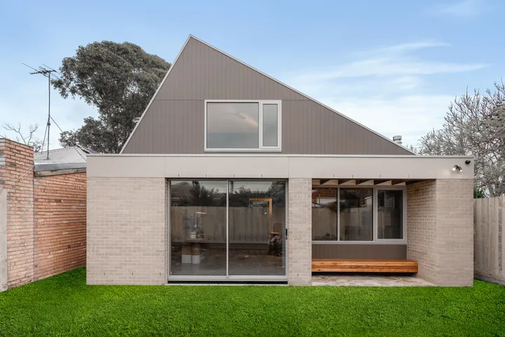 Rear exterior of contemporary Kew home with gabled roof, brick base, sliding doors and lawn