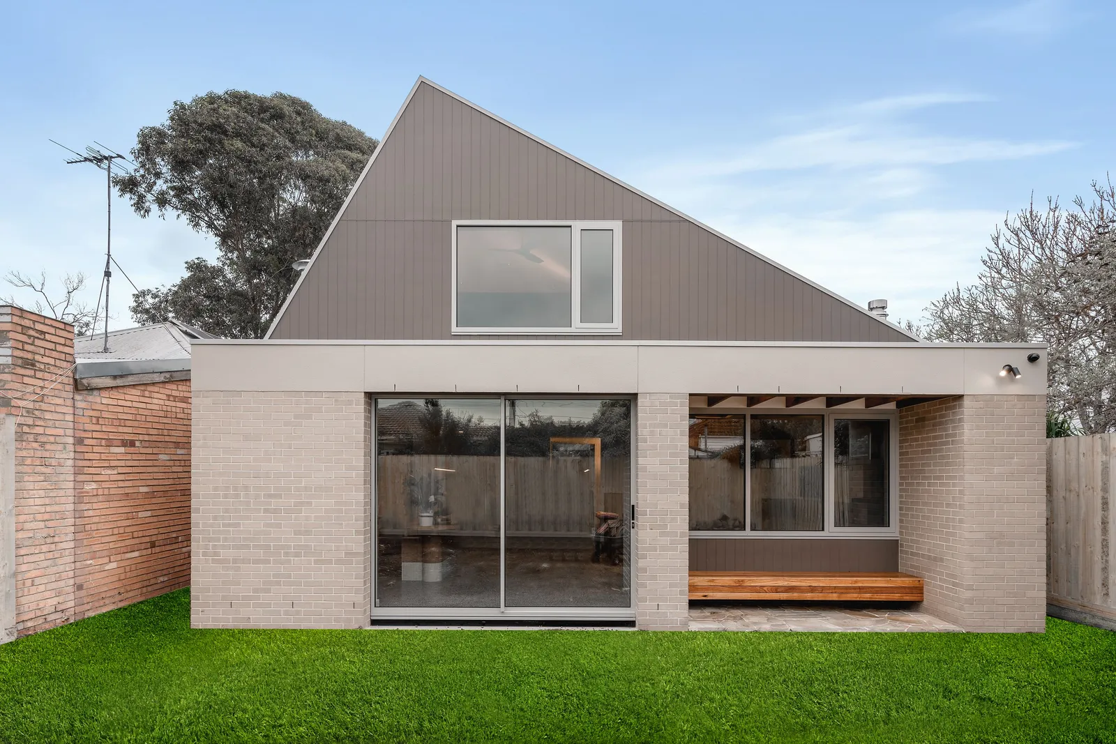 Rear exterior of contemporary Kew home with gabled roof, brick base, sliding doors and lawn