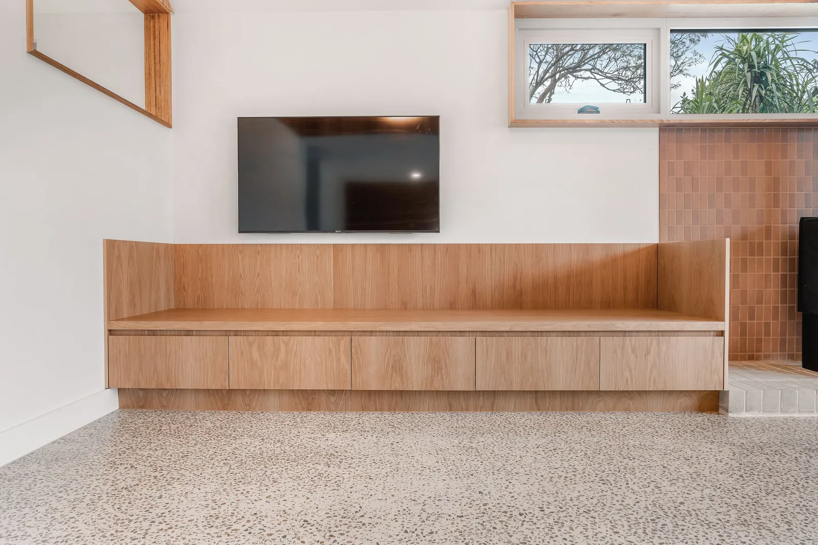 Lounge room with built-in timber bench seat, wall-mounted TV and terrazzo floor