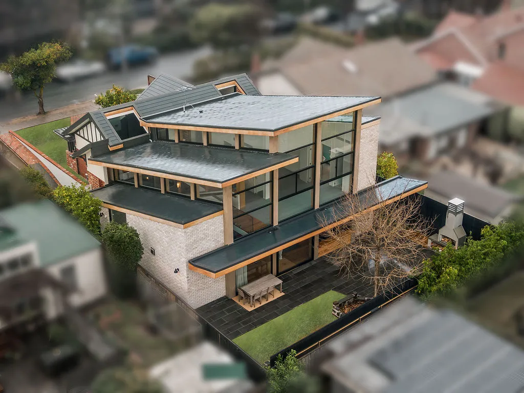 Aerial drone view of multi-level brick and timber home with zinc roof and landscaped garden