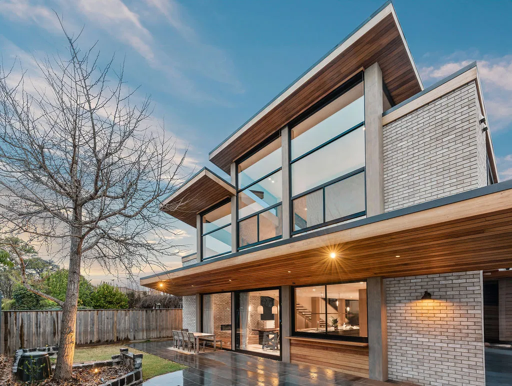 Rear exterior of contemporary Hawthorn home at dusk with timber soffit, brick facade and illuminated interior