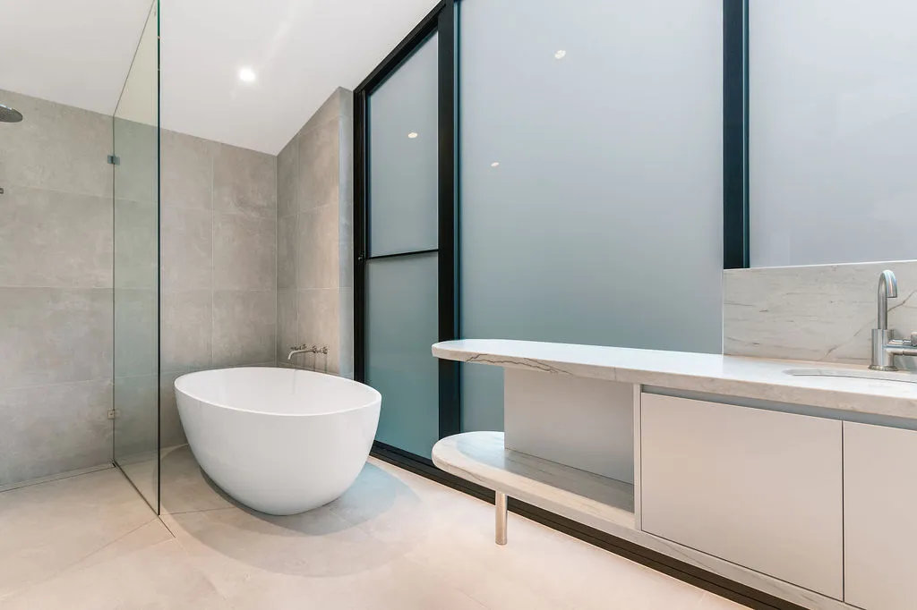 Modern ensuite with freestanding oval bath, glass shower screen and marble vanity bench