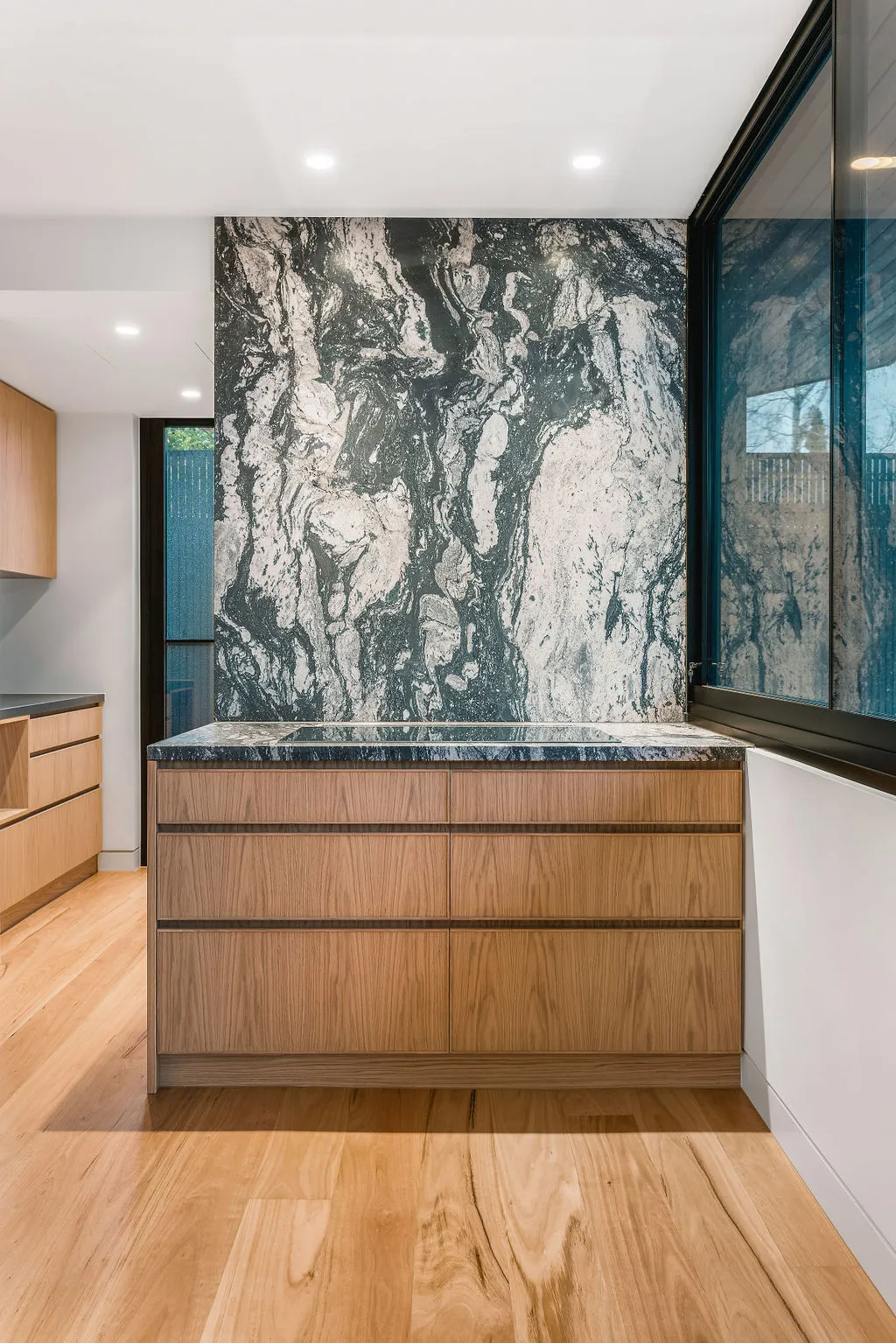 Modern kitchen island with dramatic dark marble splashback and timber cabinetry on hardwood floors