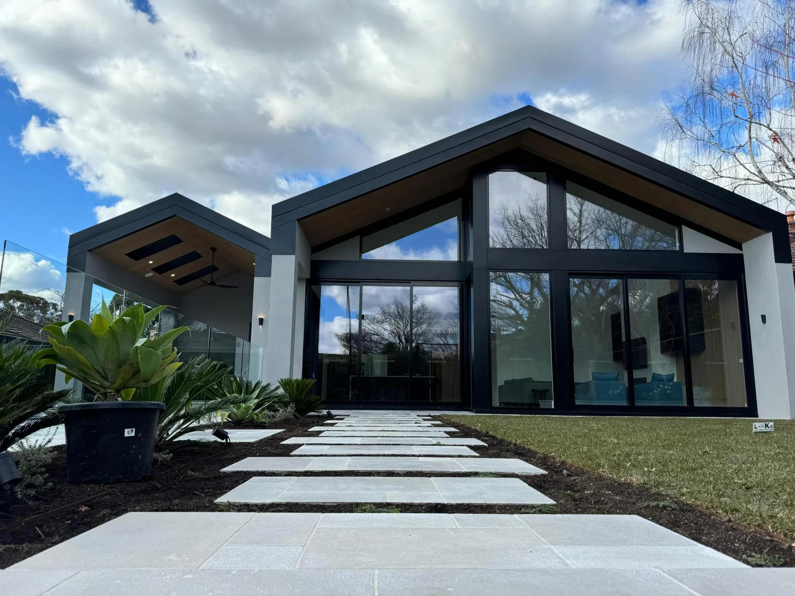 Double-gable home front exterior with large glazed gable facade, stone path and landscaping