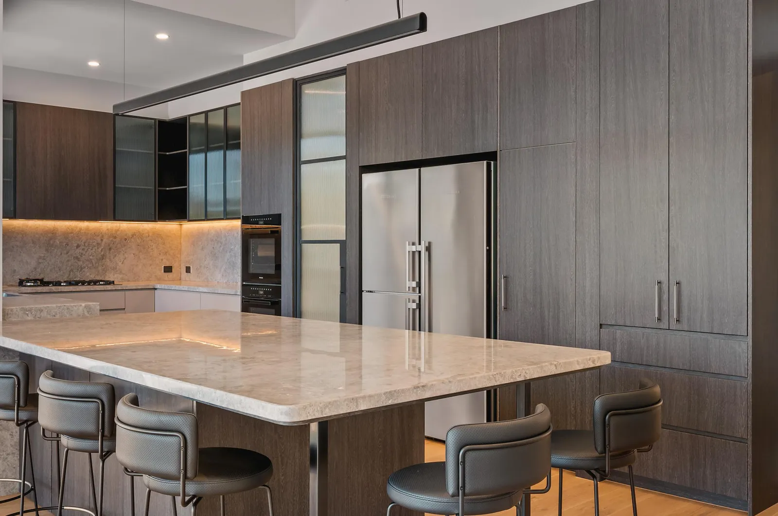 Contemporary kitchen with marble island bench, dark timber cabinetry and bar stools
