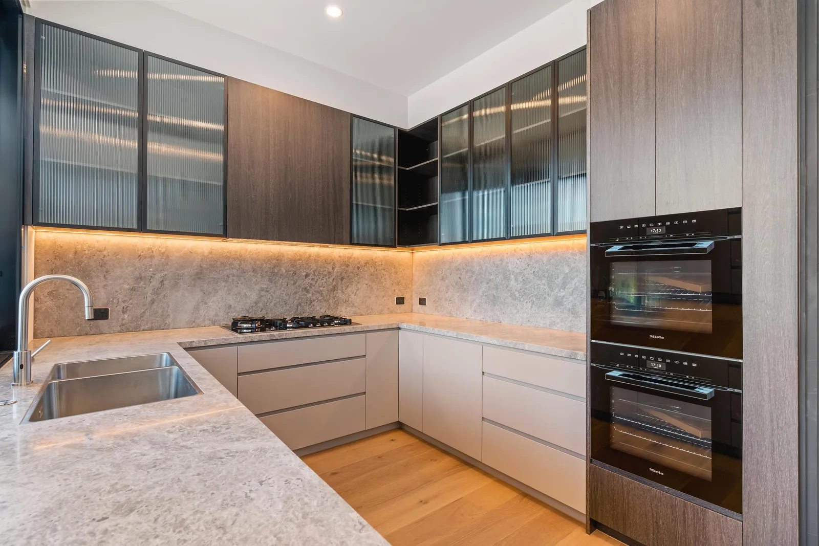 Modern kitchen with timber and glass upper cabinets, stone benchtop, Miele ovens and gas cooktop