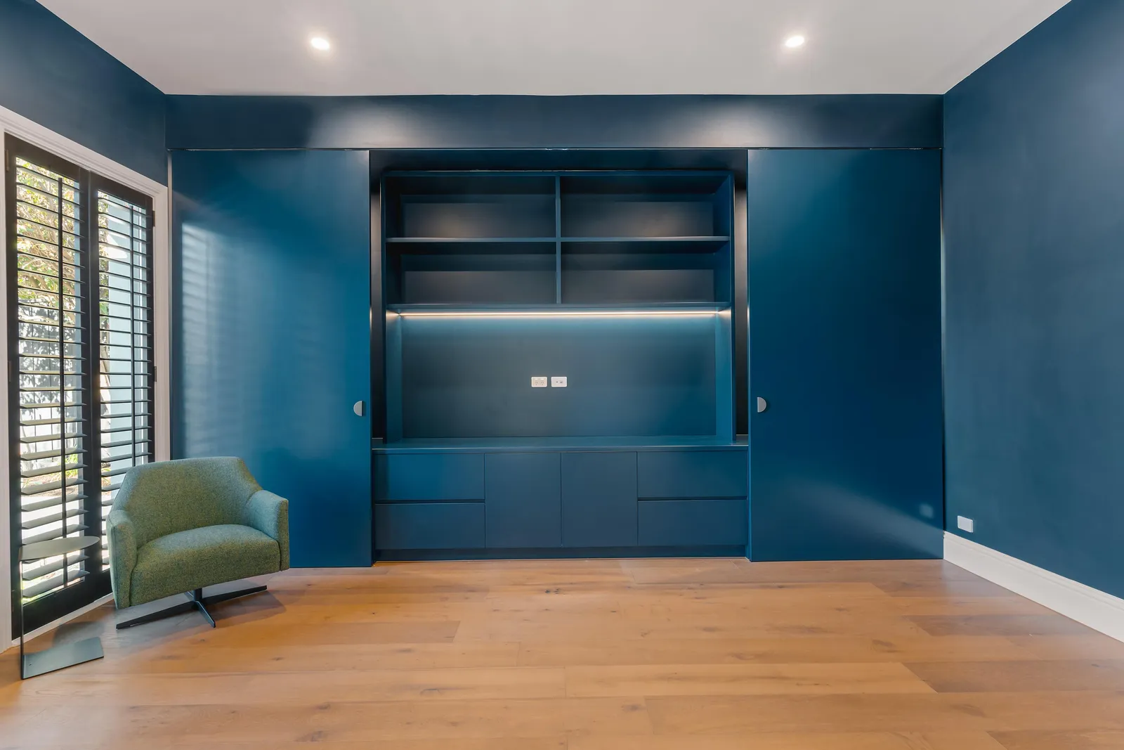 Navy living room with built-in cabinetry, shelving, and a single green armchair