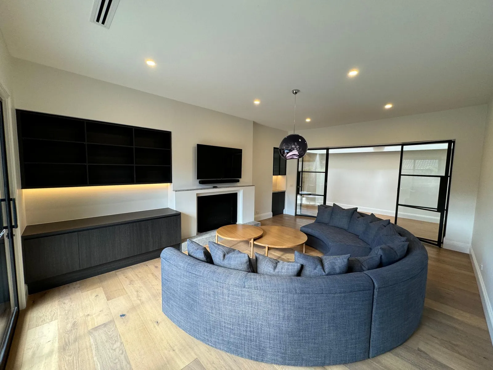 Contemporary lounge with curved grey sectional sofa, built-in shelving, fireplace, and timber floors