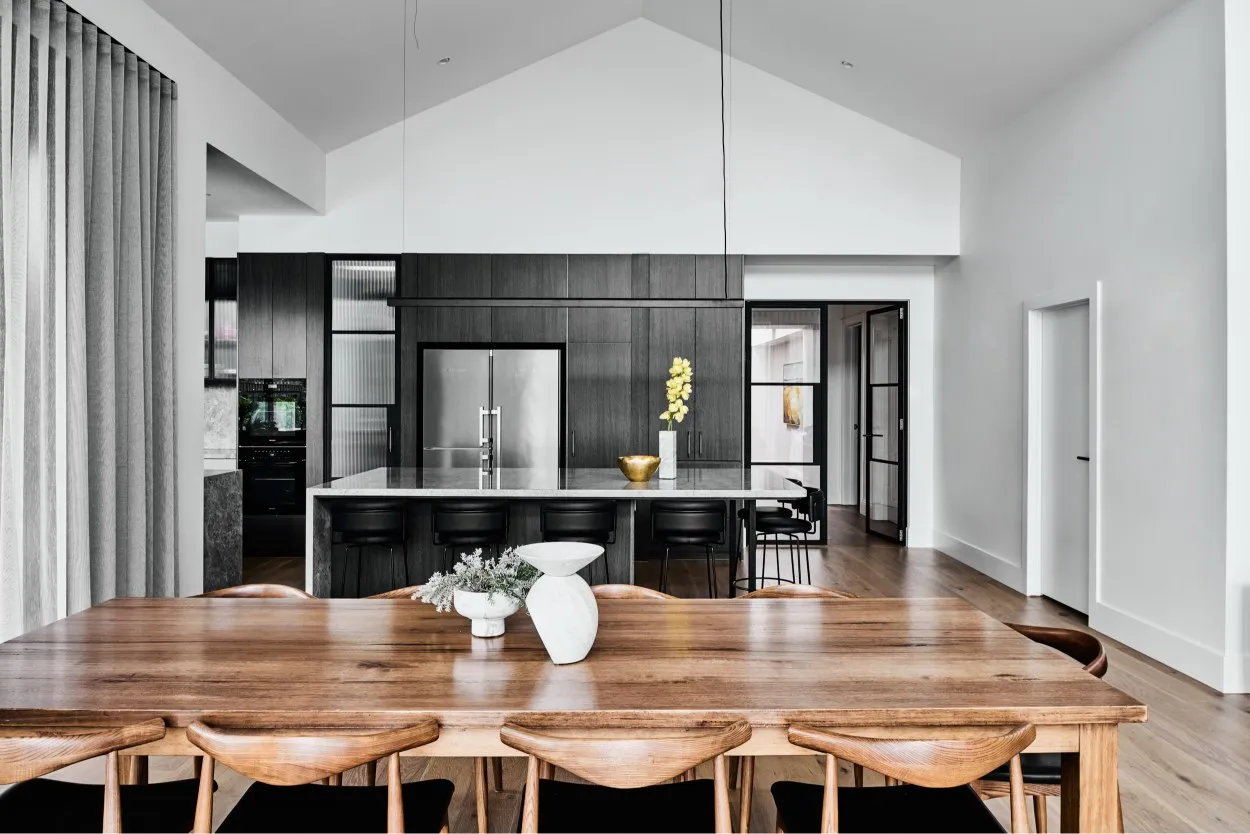 Open-plan kitchen and dining with timber table, dark cabinetry and vaulted ceiling