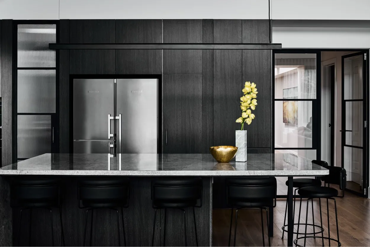 Dark timber kitchen with marble island bench, stainless steel fridge and black bar stools