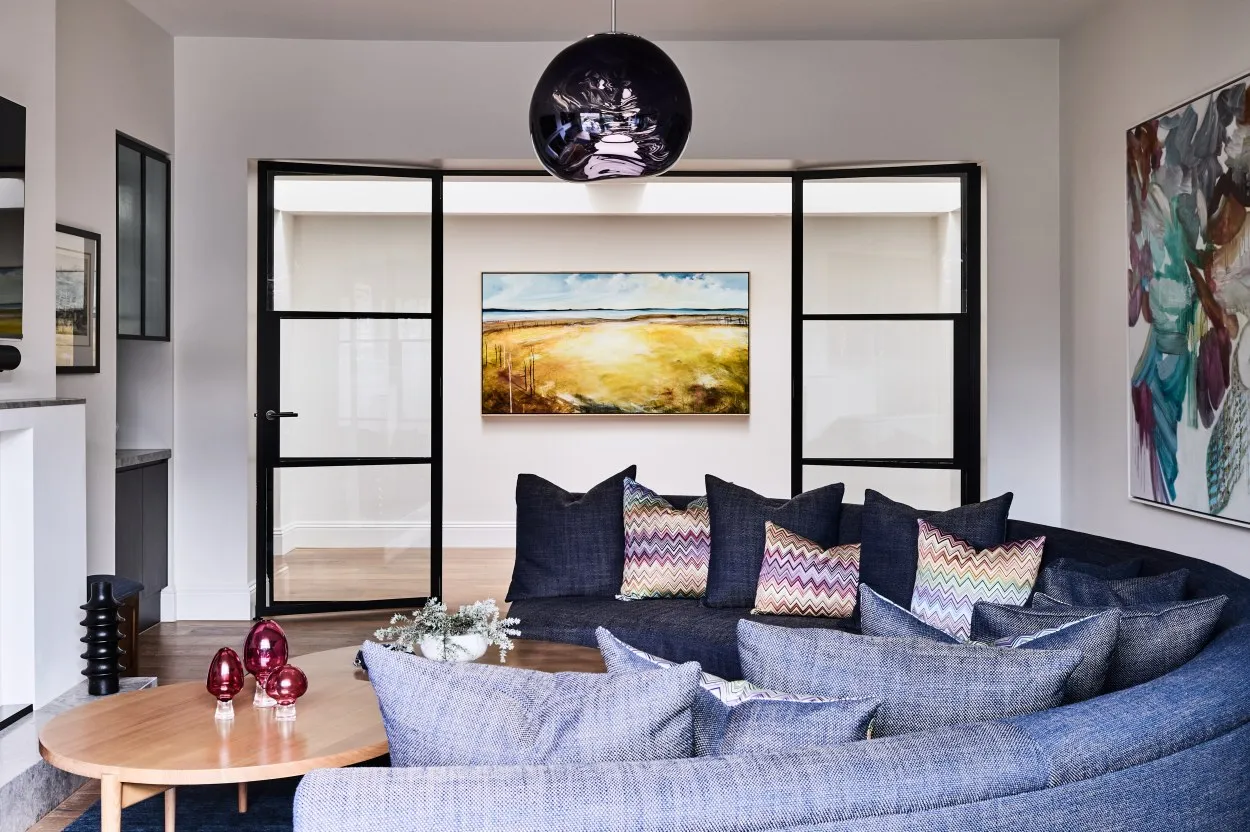 Bright lounge room with dark sofa, chevron cushions, globe pendant light and blue rug