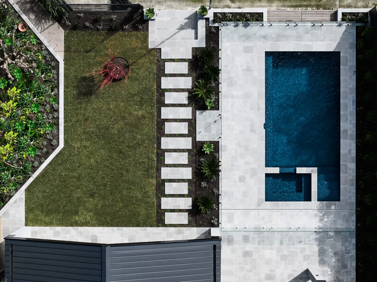 Aerial view of residential backyard with rectangular pool, stone paving and landscaped lawn