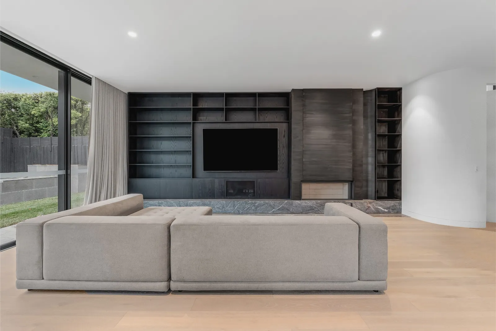 Open-plan living room with modular sofa, dark timber built-in shelving, fireplace and sliding doors