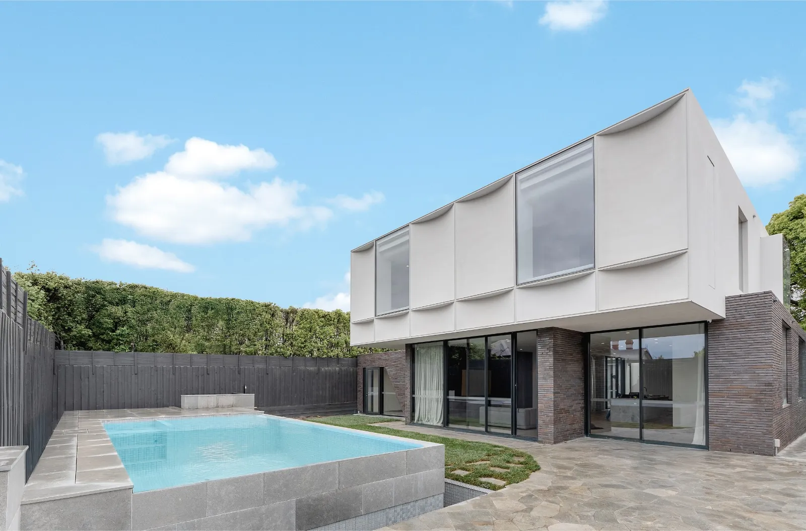 Rear garden view of modern white addition with outdoor pool and stone paving against hedge backdrop