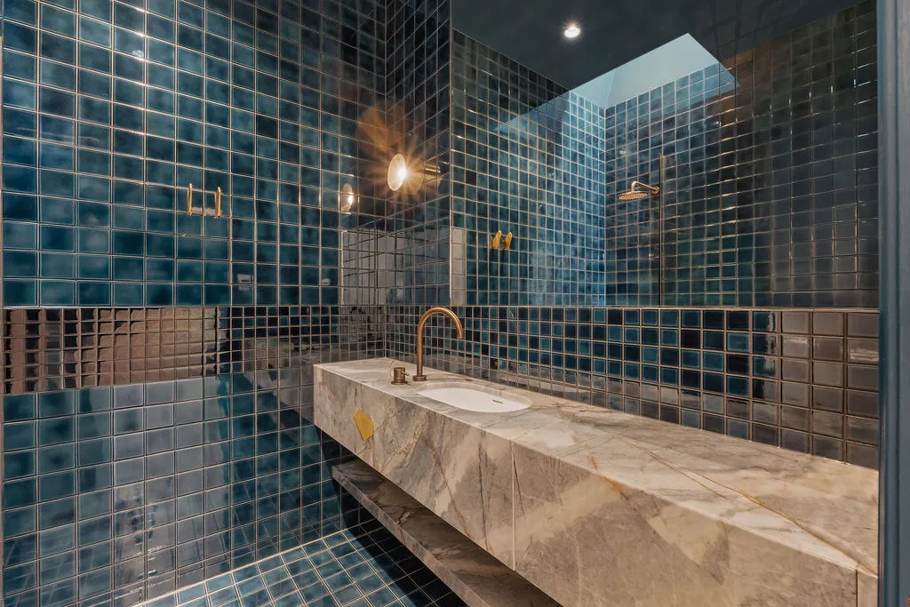 Blue tiled bathroom with marble floating vanity, brass gooseneck tap, and overhead skylight