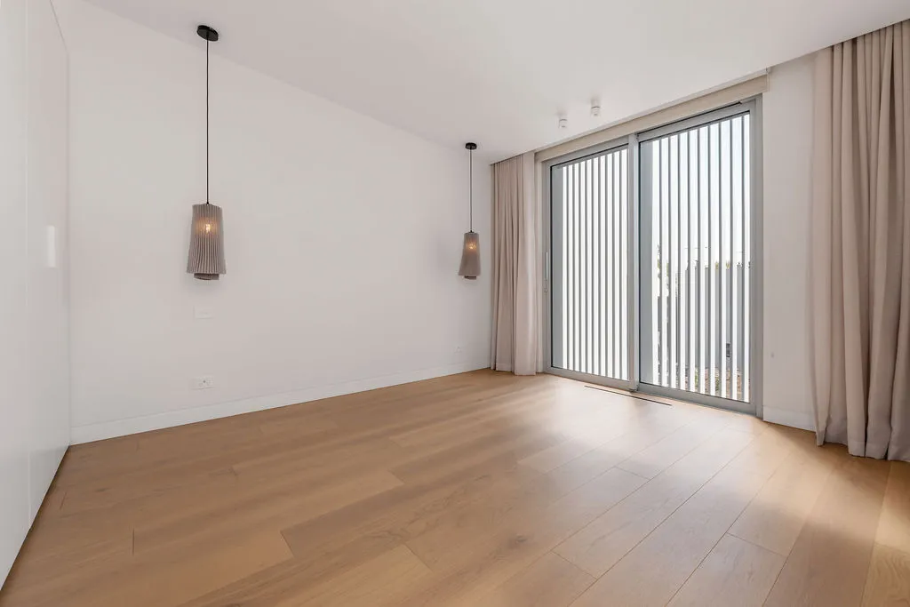 Minimalist bedroom with timber floors, pendant lights, sheer curtains, and sliding glass door to balcony