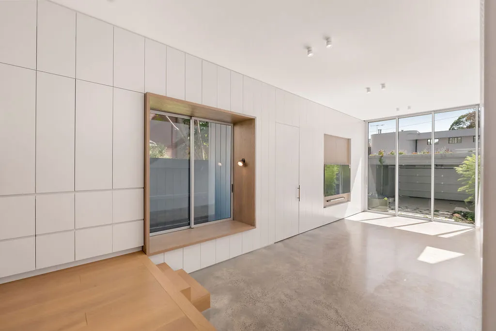Open-plan living space with polished concrete floors, white joinery wall, and glazed rear doors