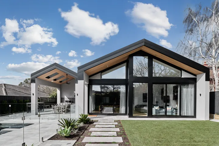 Contemporary home with pitched black roof, full-height glazed gable end, timber soffits and garden stepping stones