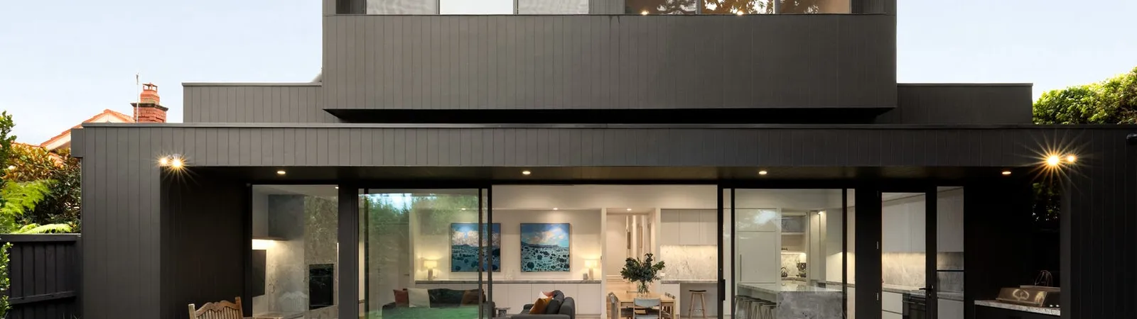 Black timber-clad two-storey rear extension with full-height glazing opening to a level lawn