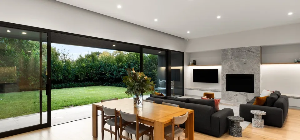 Living and dining space opening through stacking glass sliders to the garden