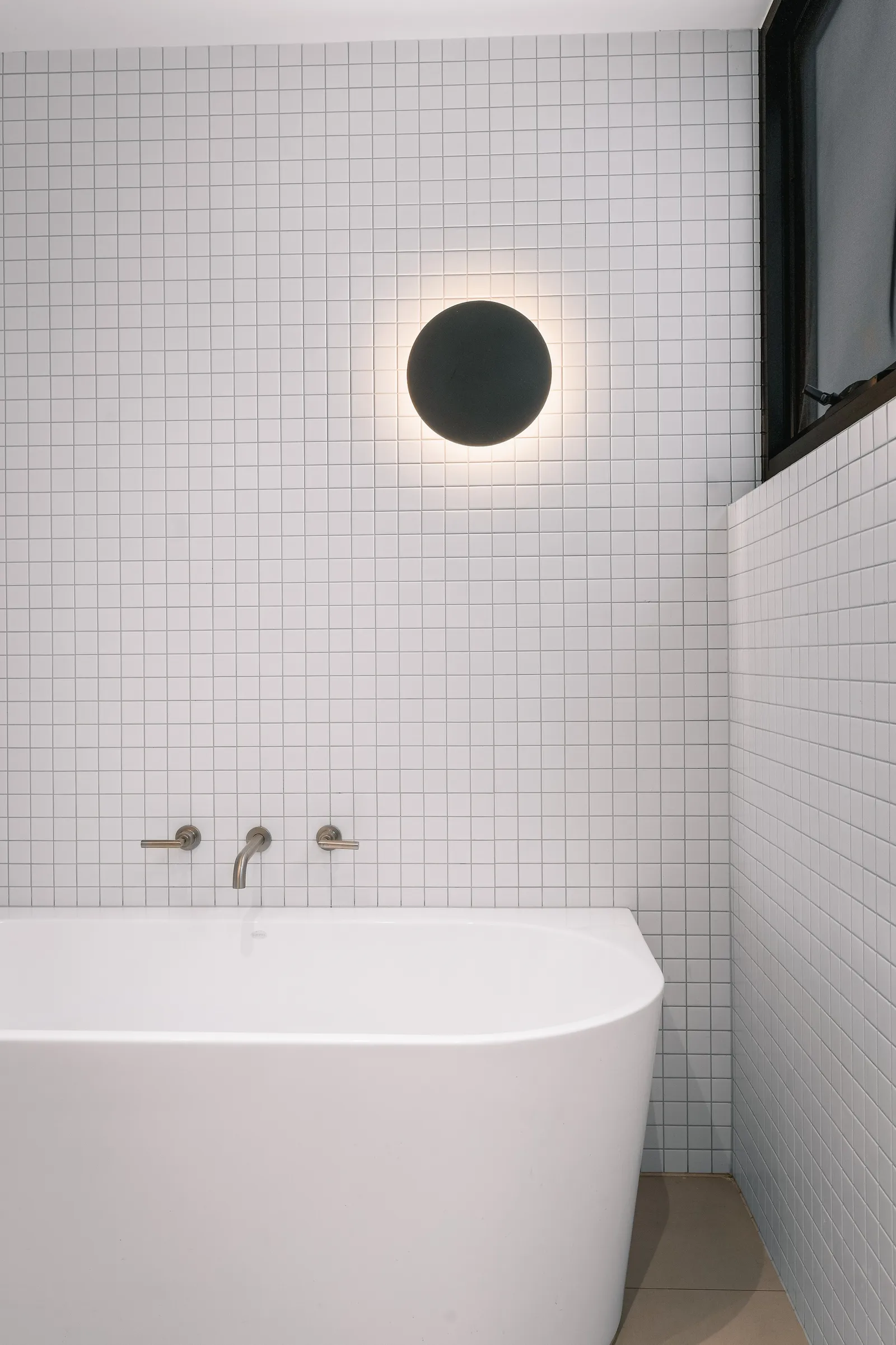 White freestanding bath against square grid tiles with round sconce