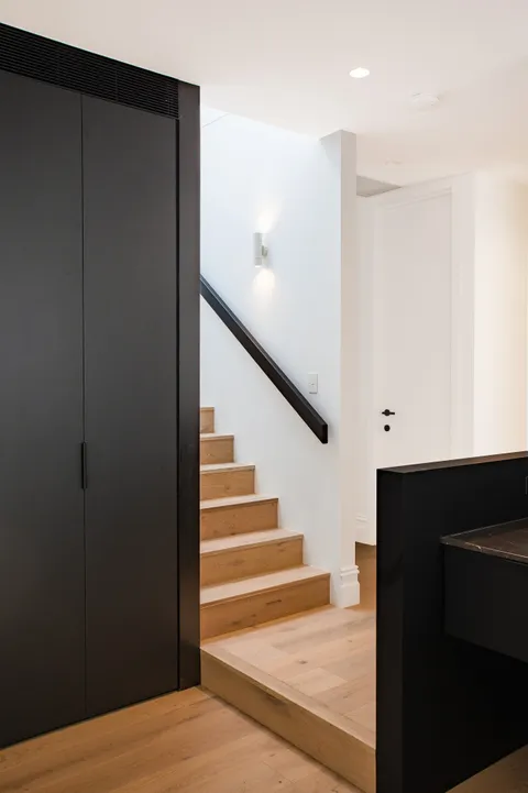 Timber staircase with black handrail beside full height black joinery