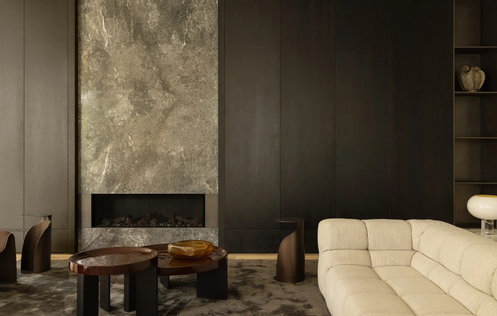 Luxury living room with stone fireplace surround, cream sofa, dark timber panelling, and designer furniture