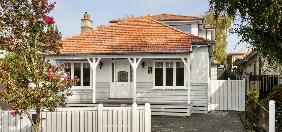White weatherboard bungalow facade with terracotta tile roof, front verandah and white picket fence in Kew