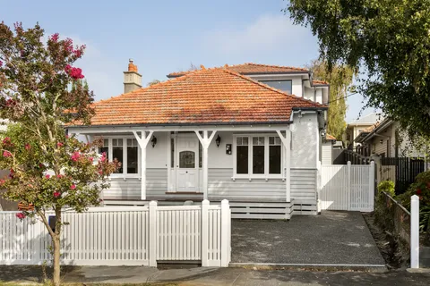 White weatherboard bungalow facade with terracotta tile roof, front verandah and white picket fence in Kew
