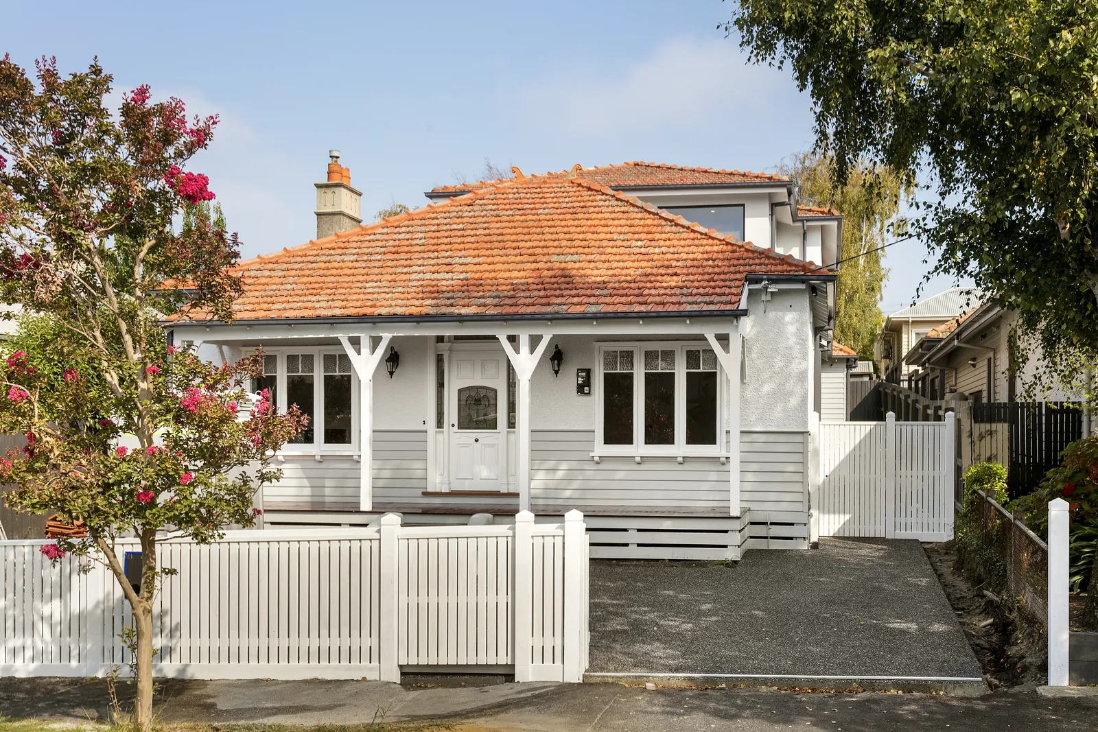 White weatherboard bungalow facade with terracotta tile roof, front verandah and white picket fence in Kew