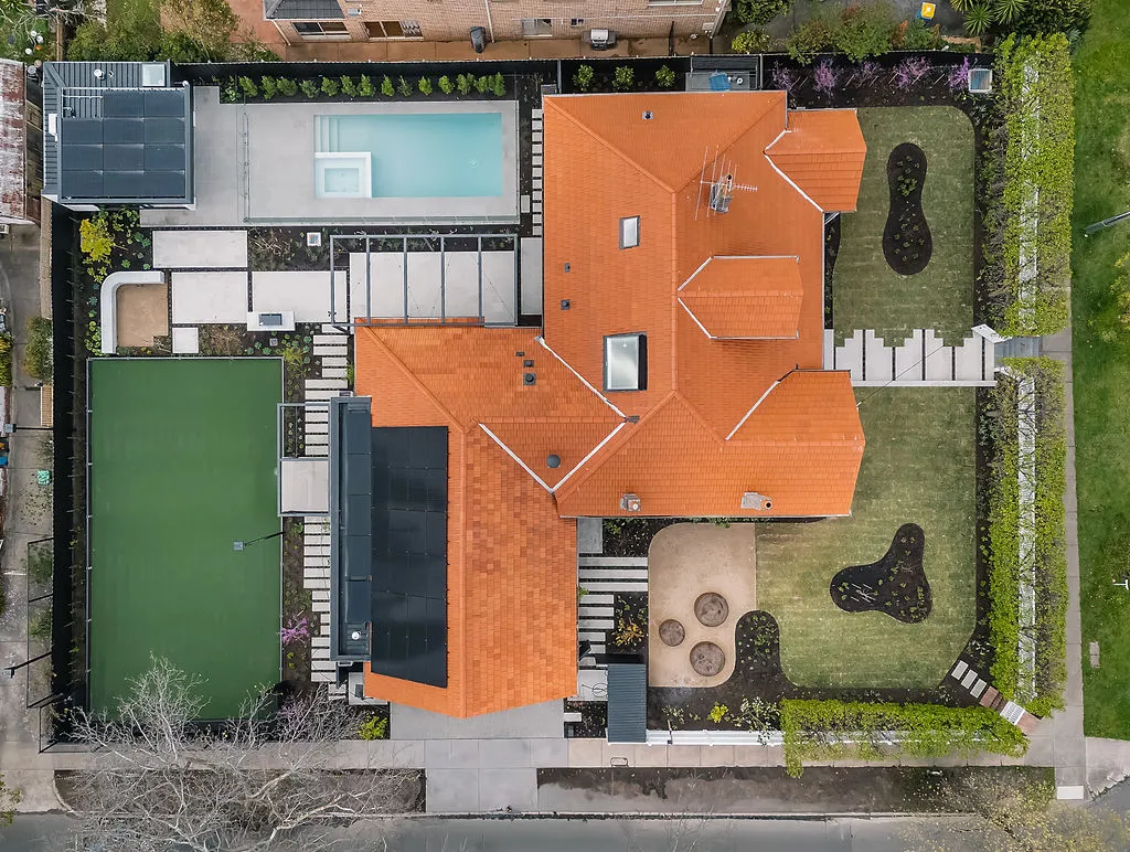 Aerial overhead view of large suburban home with terracotta tiled roof, pool, tennis court and landscaped grounds