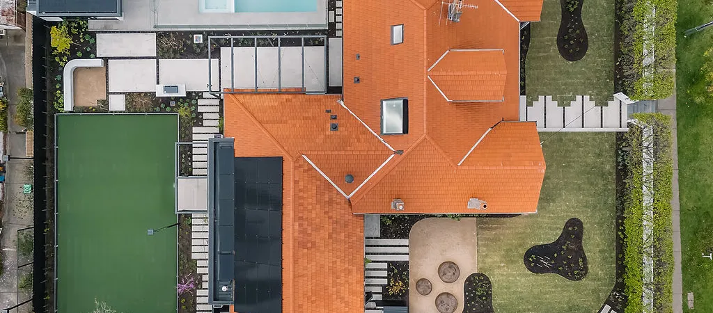 Aerial overhead view of large suburban home with terracotta tiled roof, pool, tennis court and landscaped grounds