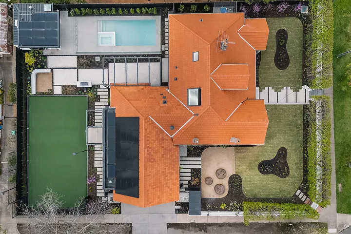 Aerial overhead view of large suburban home with terracotta tiled roof, pool, tennis court and landscaped grounds