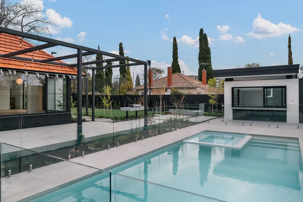 Outdoor pool with glass fencing, steel pergola, and contemporary pool house