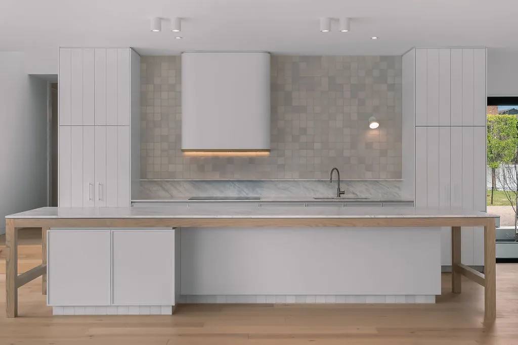 Sleek white kitchen with large island, timber dining table extension, tiled splashback and rangehood