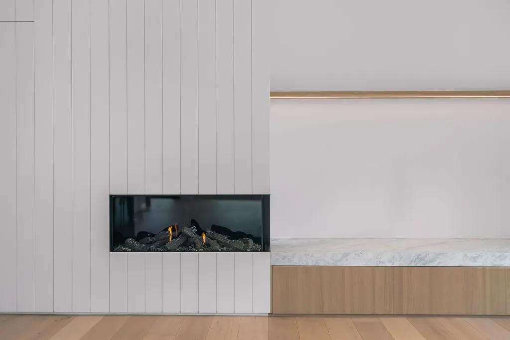 Linear gas fireplace set into ribbed white panelled wall with marble bench and timber cabinetry