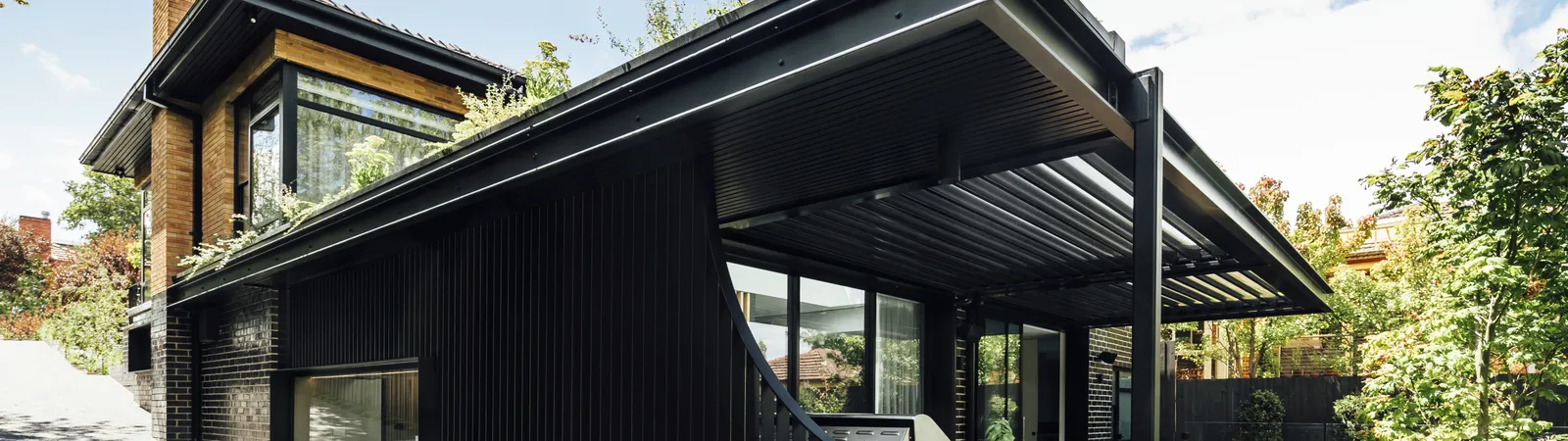 Black clad contemporary home exterior with pergola and rooftop greenery