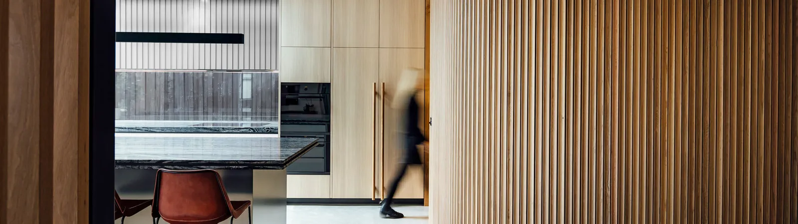 Curved timber slat wall feature beside dark marble kitchen island with leather bar stools
