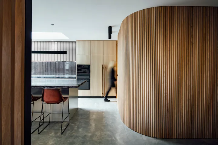 Curved timber slat wall feature beside dark marble kitchen island with leather bar stools