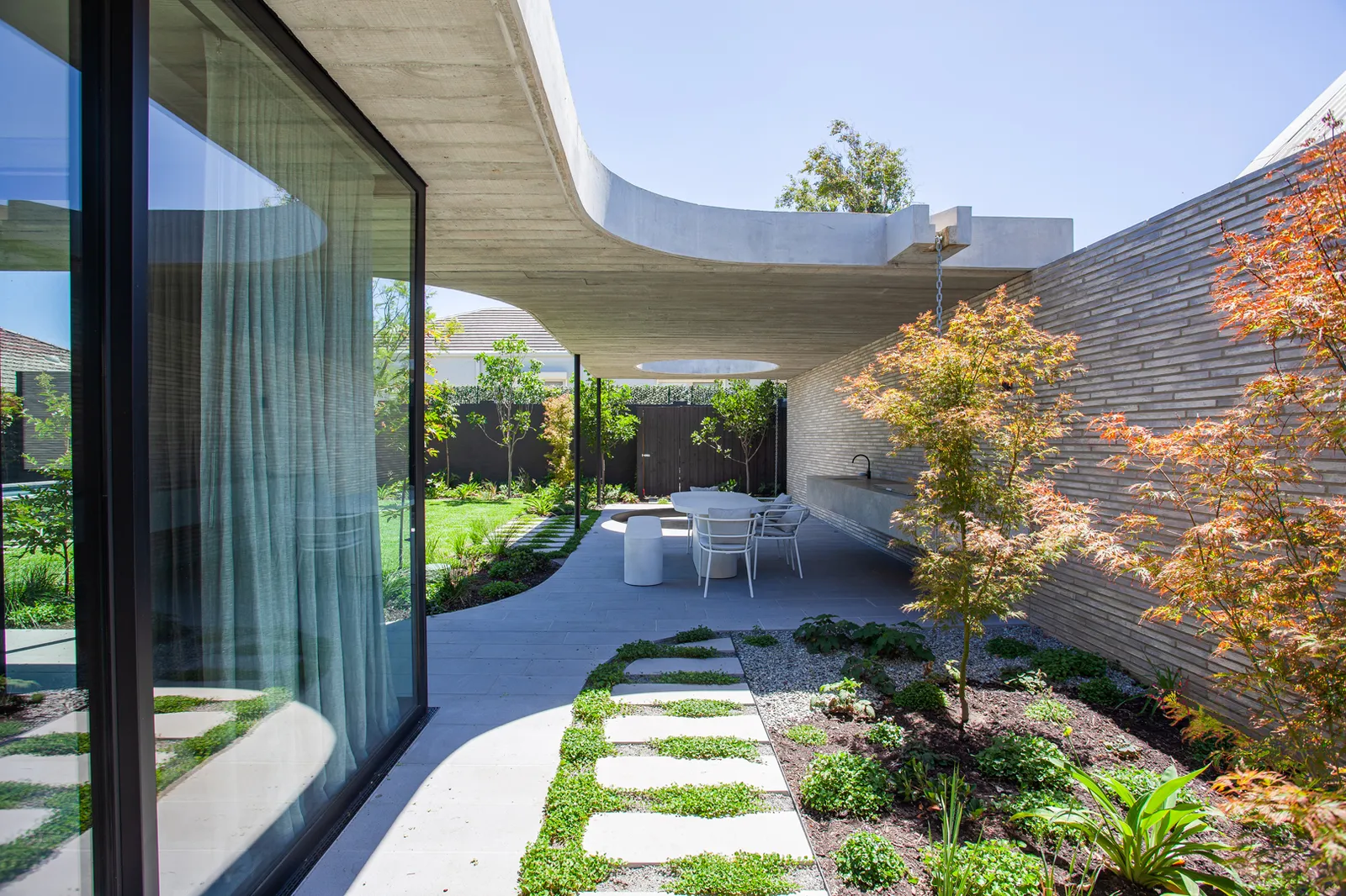 Covered outdoor terrace with stepping stone path, Japanese maple, alfresco dining, and curved concrete roof