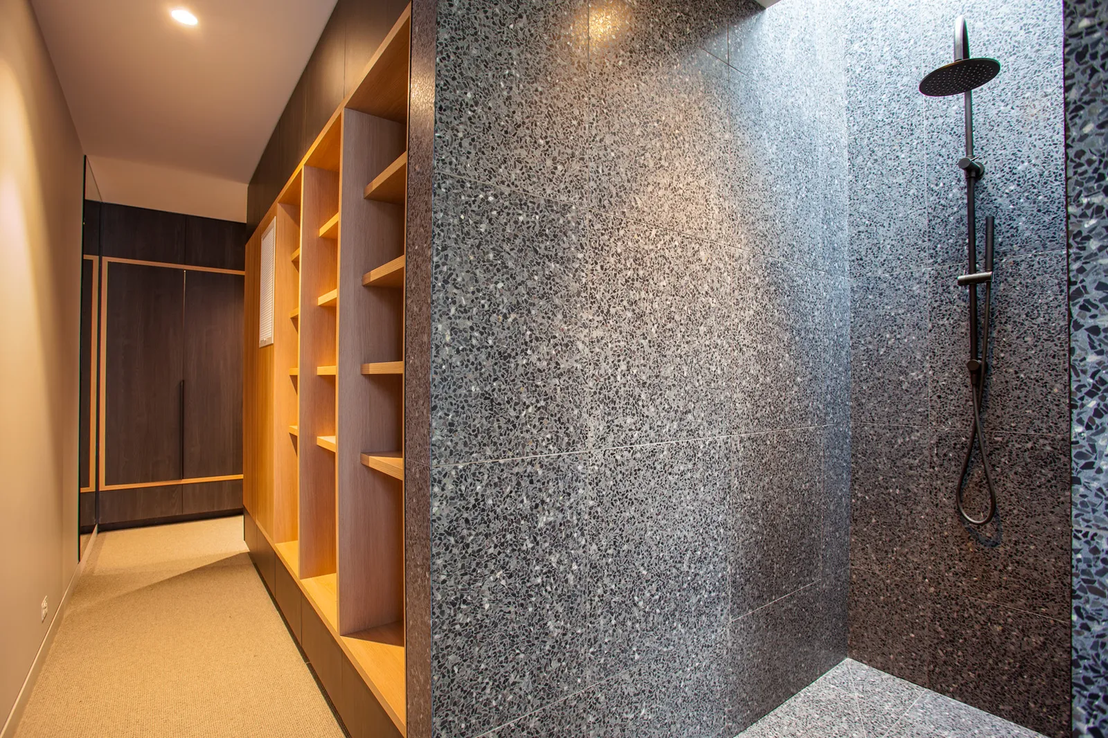 Walk-in robe with open timber shelving adjoining terrazzo-tiled shower with rain head