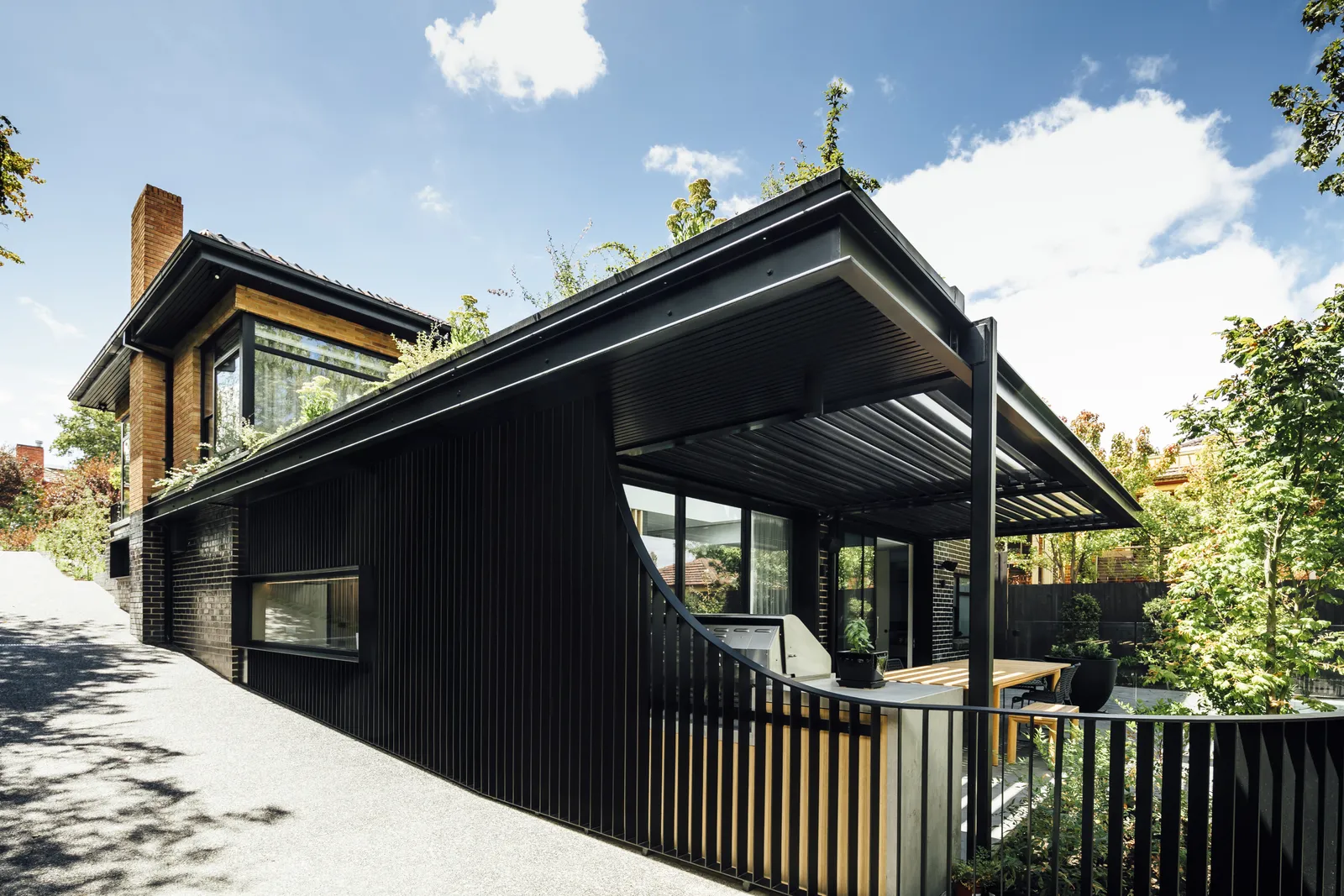 Modern black clad home exterior with louvred pergola, green roof, and timber accents