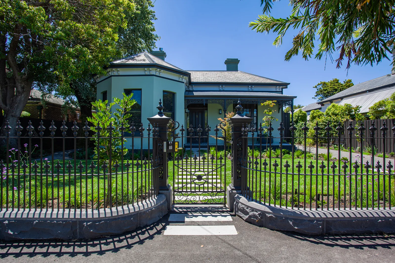 Renovated heritage home with ornate iron fence, green lawn, and bay window facade