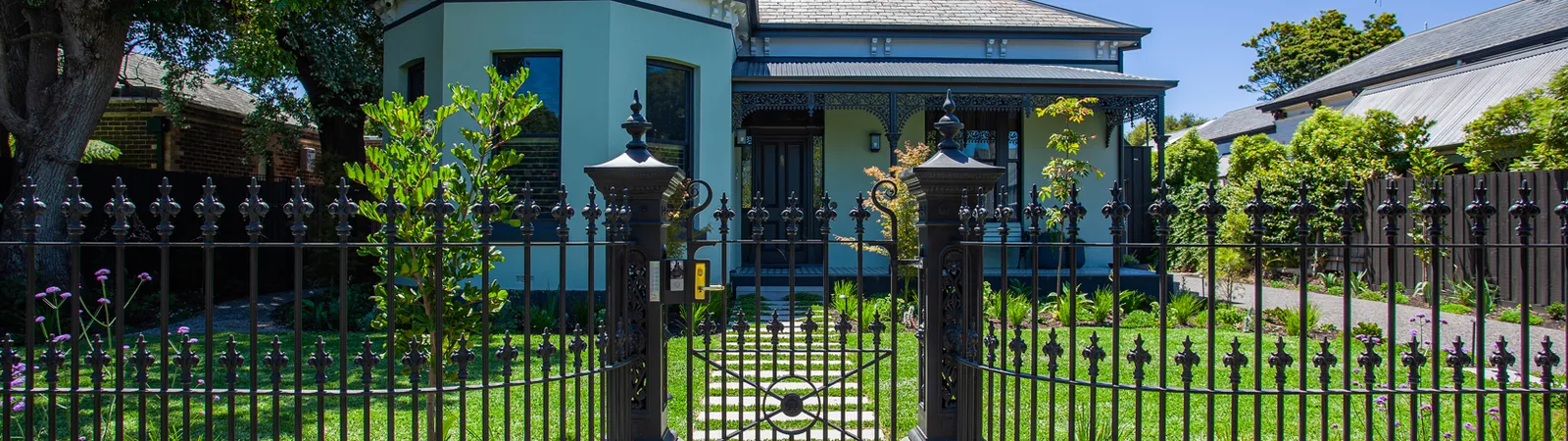 Renovated heritage home with ornate iron fence, green lawn, and bay window facade
