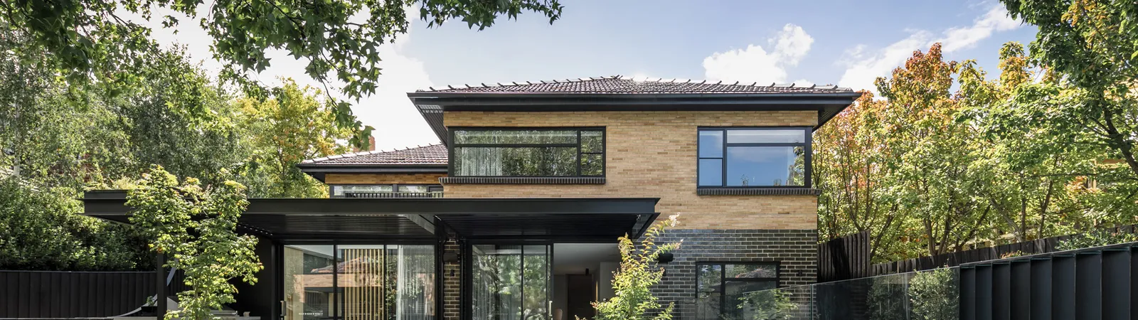 Two-storey brick and dark timber home exterior viewed from garden with pool and patio