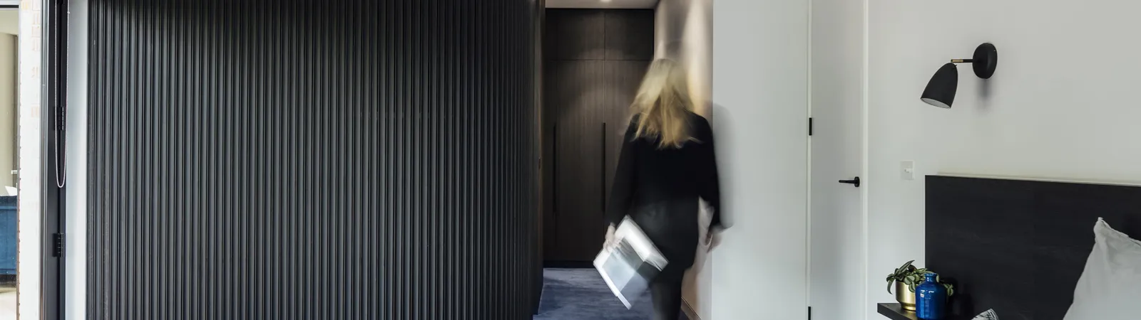 Contemporary bedroom with dark fluted curved wardrobe, blue carpet and figure in motion