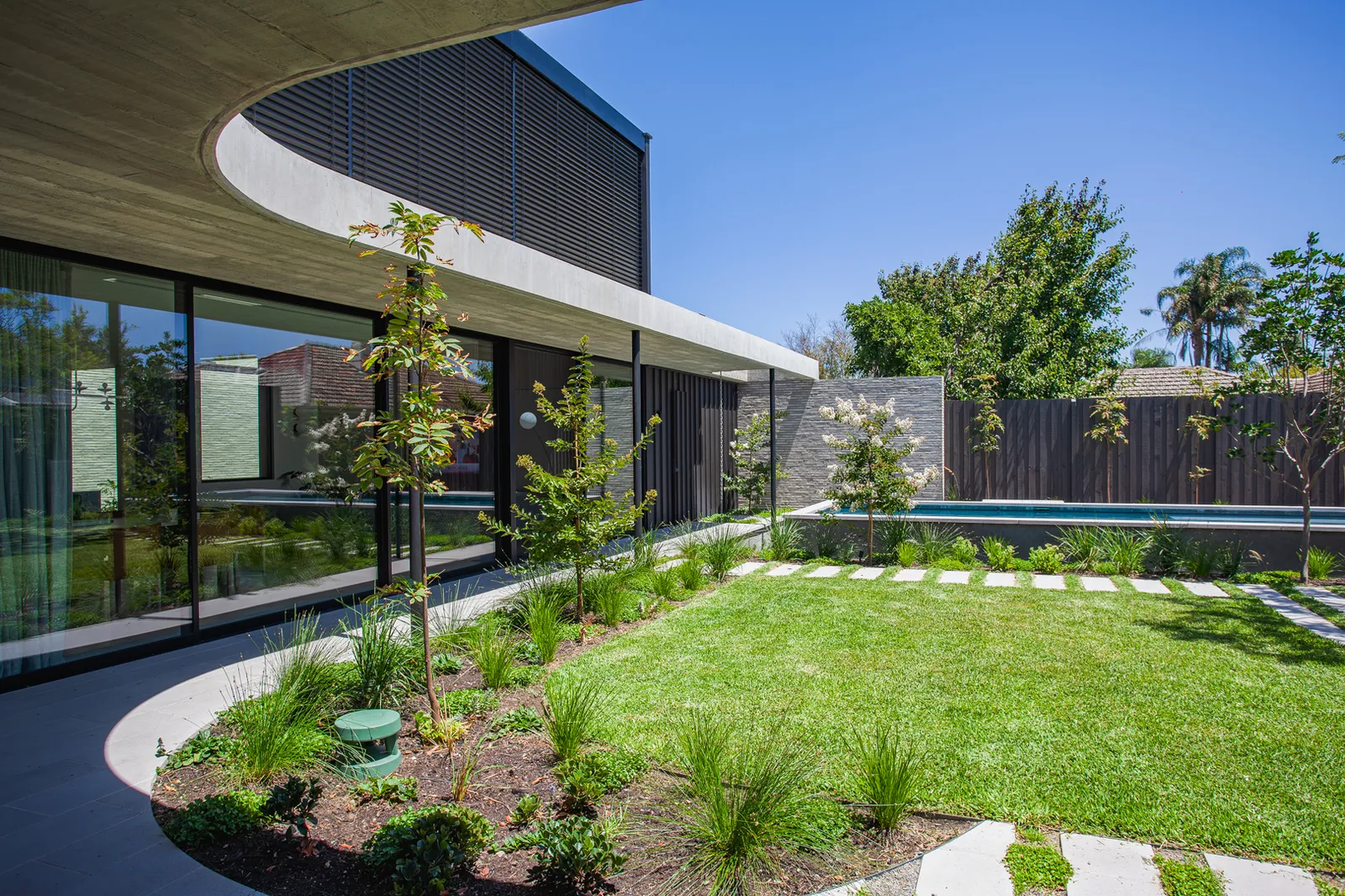 Curved concrete roof overhang above a manicured garden courtyard with pool and timber louvre facade