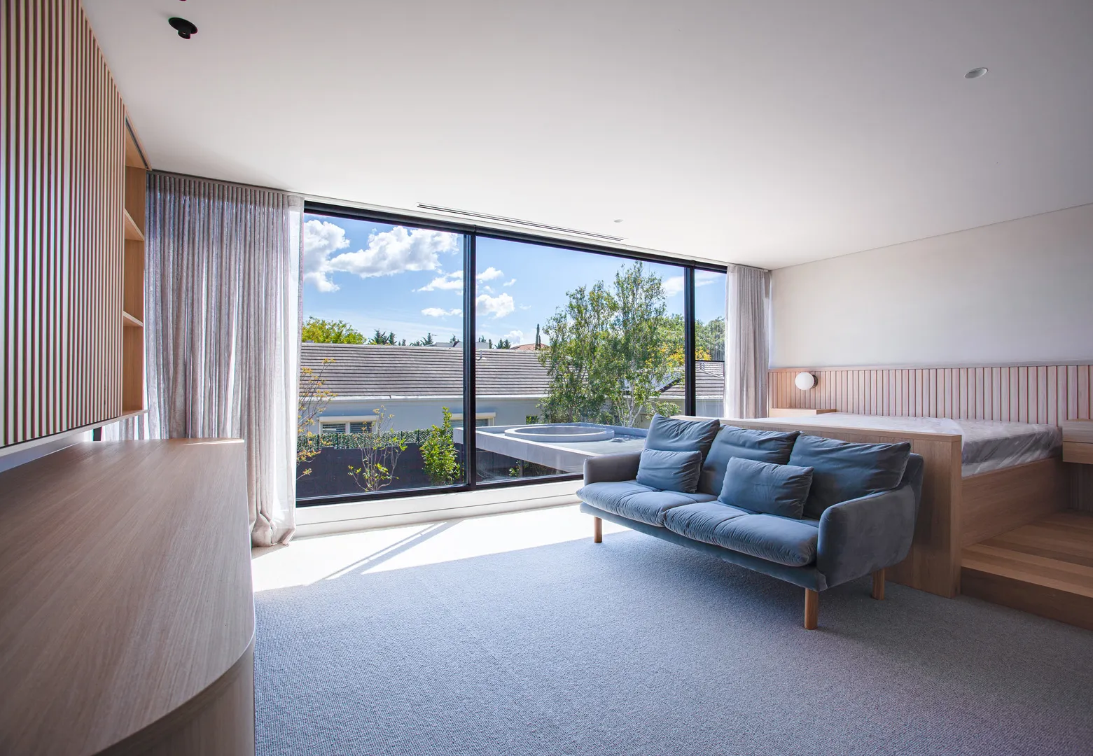 Bright living room with blue sofa, timber slat wall and floor-to-ceiling windows overlooking rooftop terrace