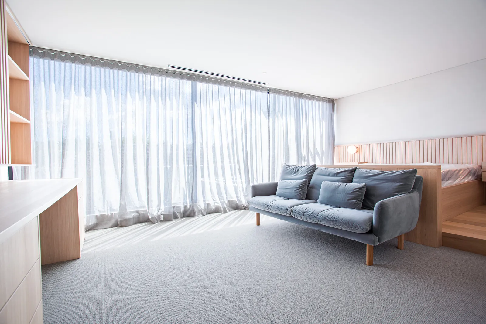 Bright bedroom sitting area with grey sofa, sheer curtains, and timber joinery