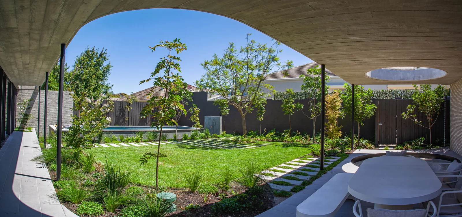 Panoramic backyard with arched concrete frame, lawn, stepping stones, pool and mature trees